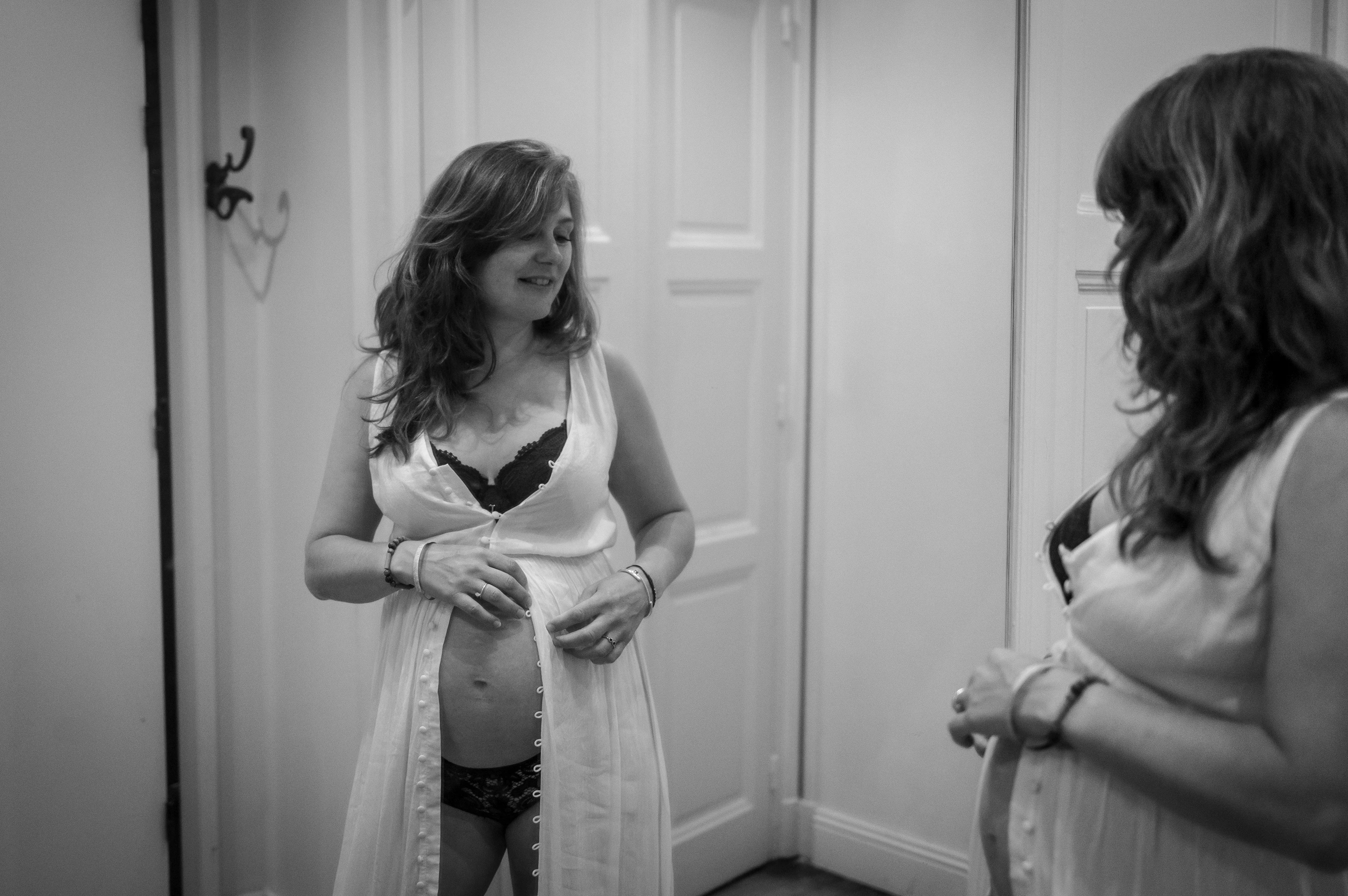 Femme enceinte en robe claire qui se regarde dans le miroir photographié par Marine Bourely Photographe