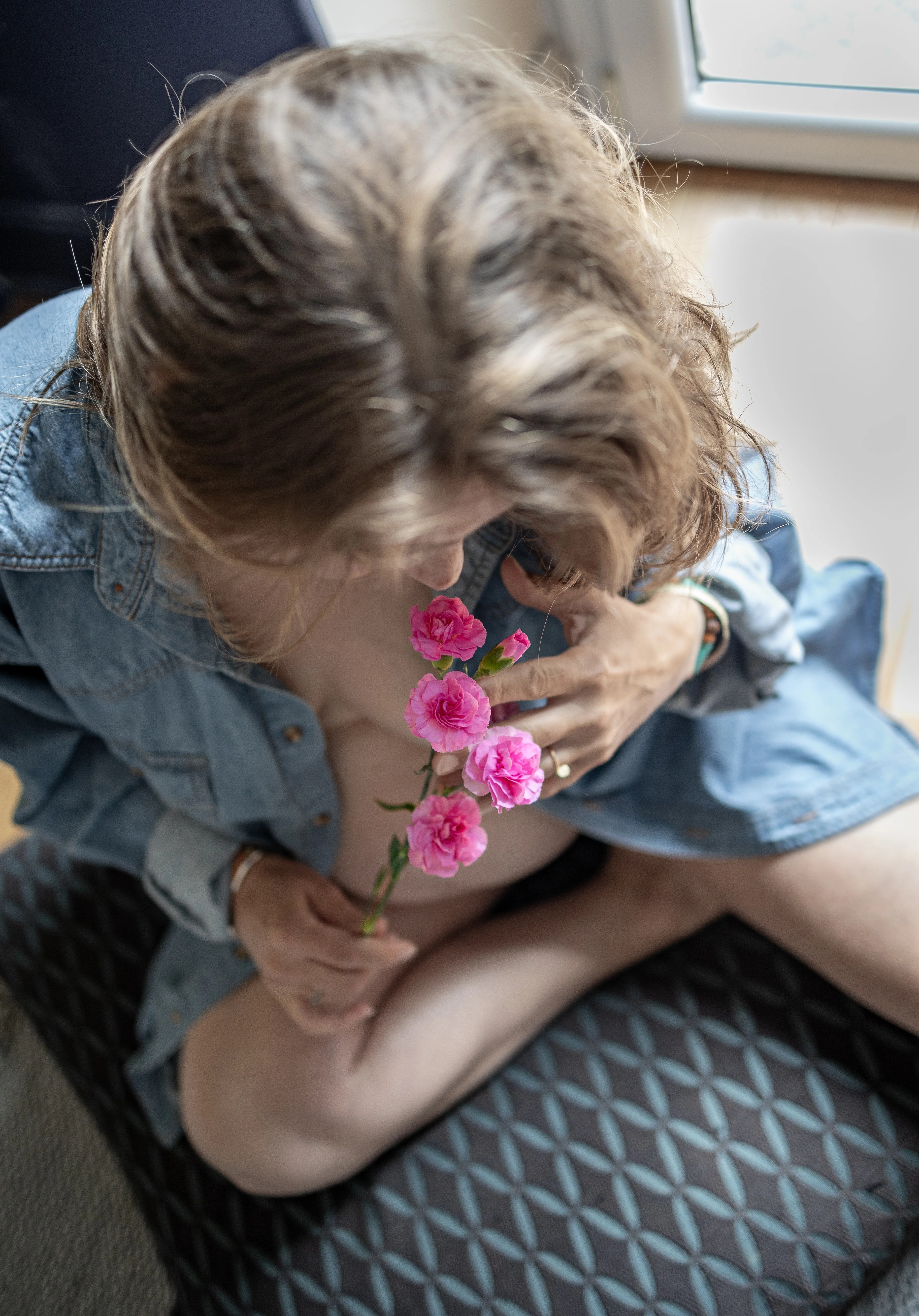 Femme enceinte avec une chemise en jean ouverte tient un bouquet de fleurs roses à la main photographiée par Marine Bourely Photographe