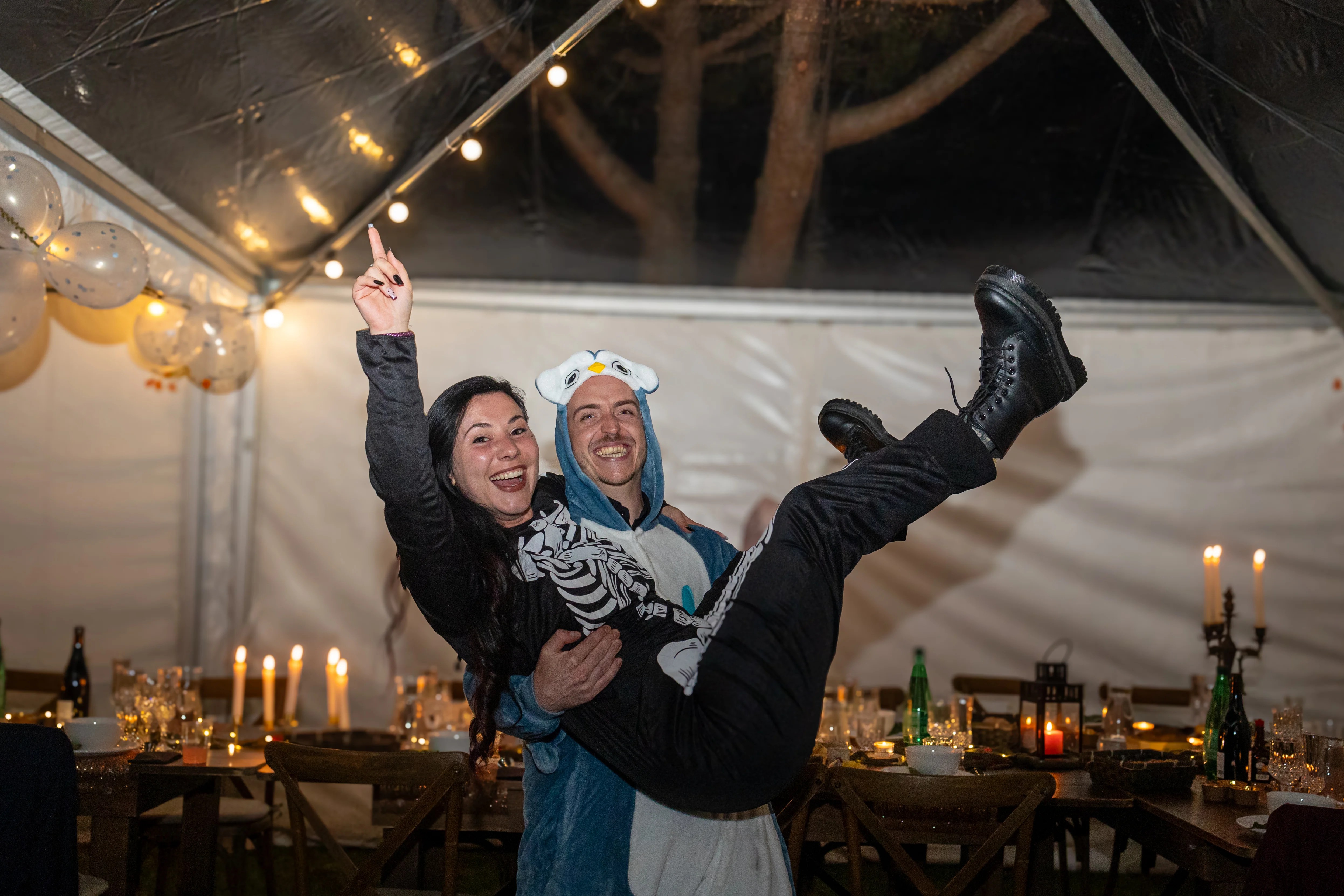 Un homme porte sa femme dans ses bras, tous deux déguisés lors d'une fête entre amis photographiés par Marine Bourely Photographe