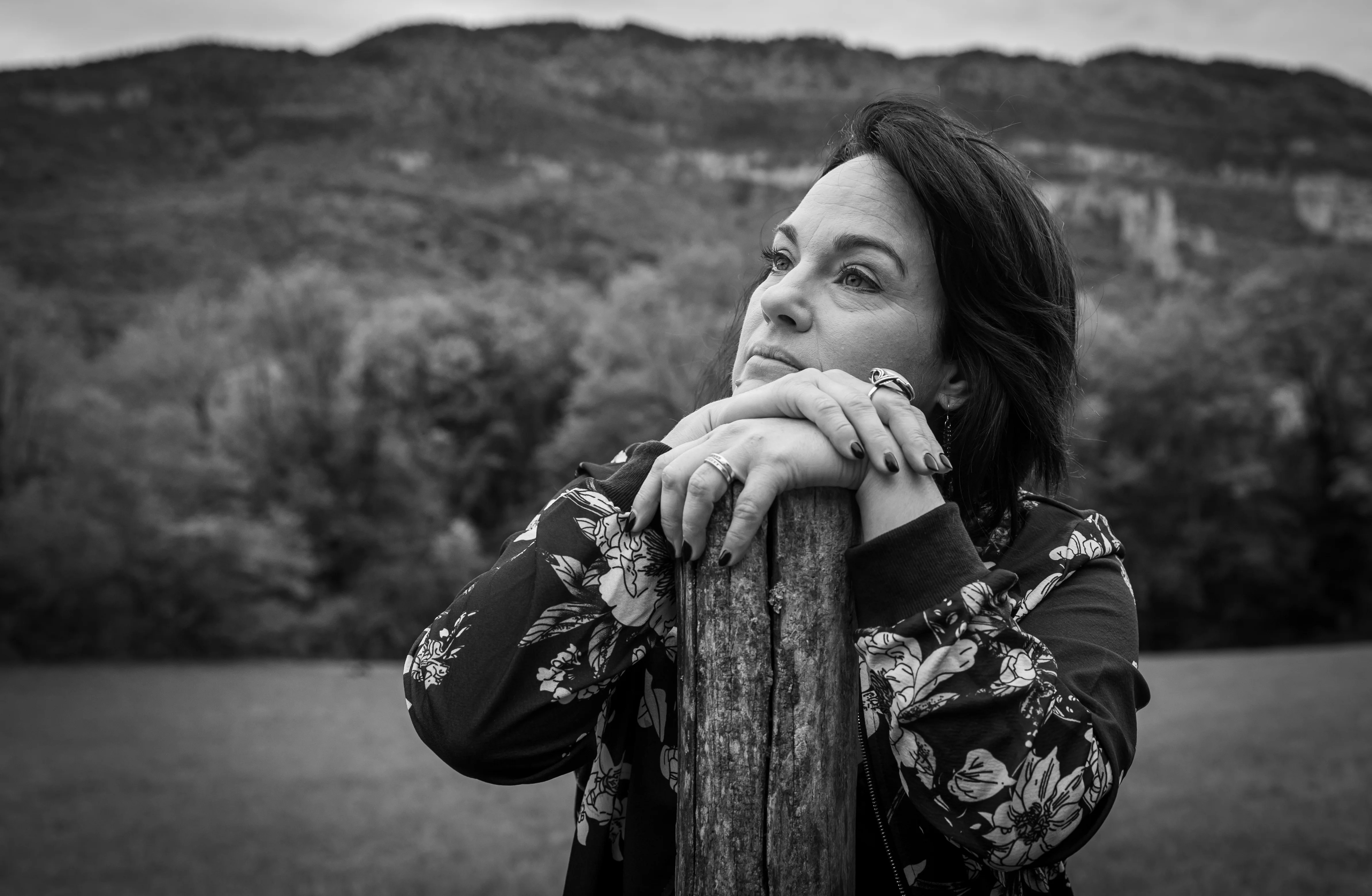 Femme pensive accoudée à un poteau en bois devant la montagne photographiée par Marine Bourely Photographe