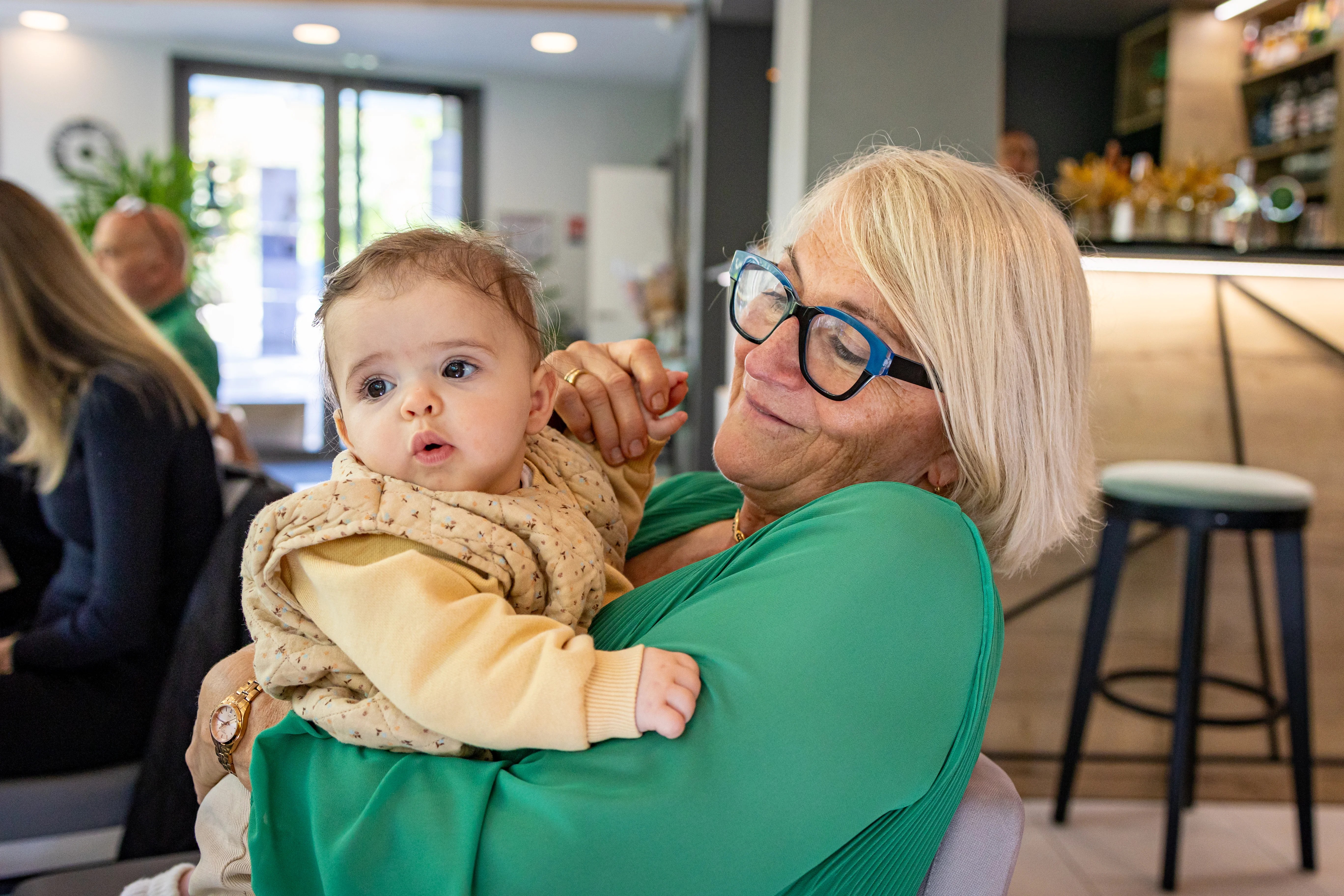 Un bébé dans les bras de sa grand-mère lors d'une fête de famille photographiés par Marine Bourely Photographe