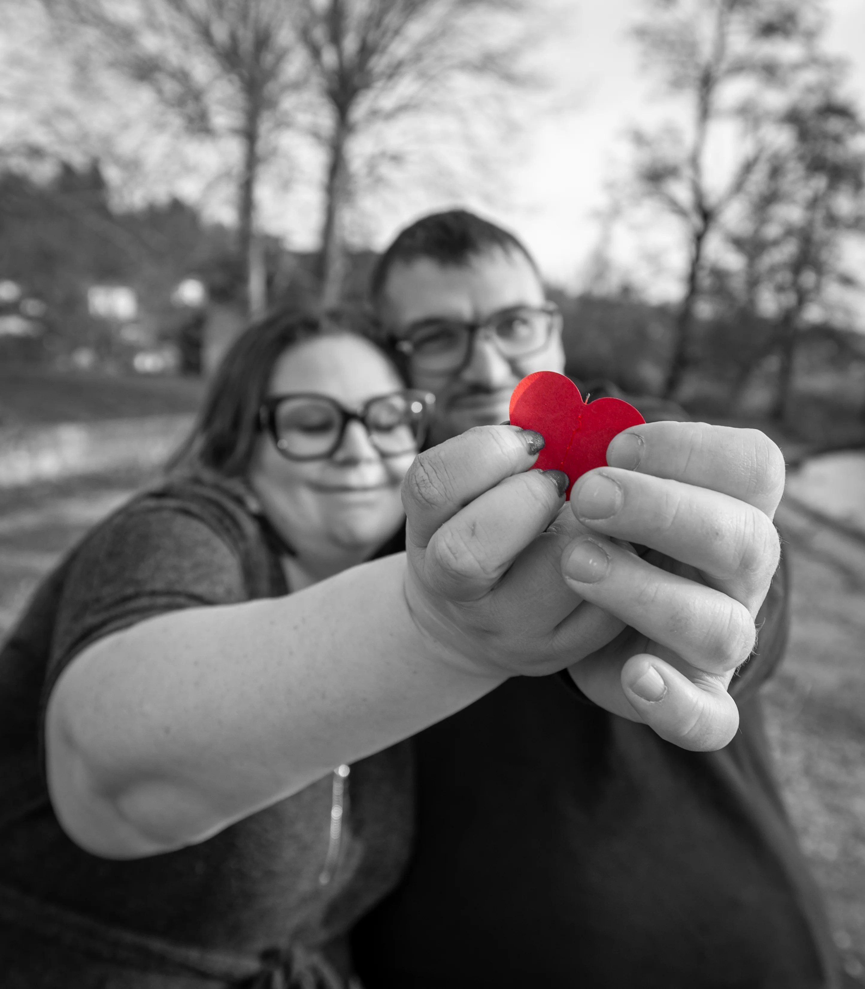 Couple en noir et blanc s'enlaçant et tenant un cœur rouge en papier photographié par Marine Bourely Photographe