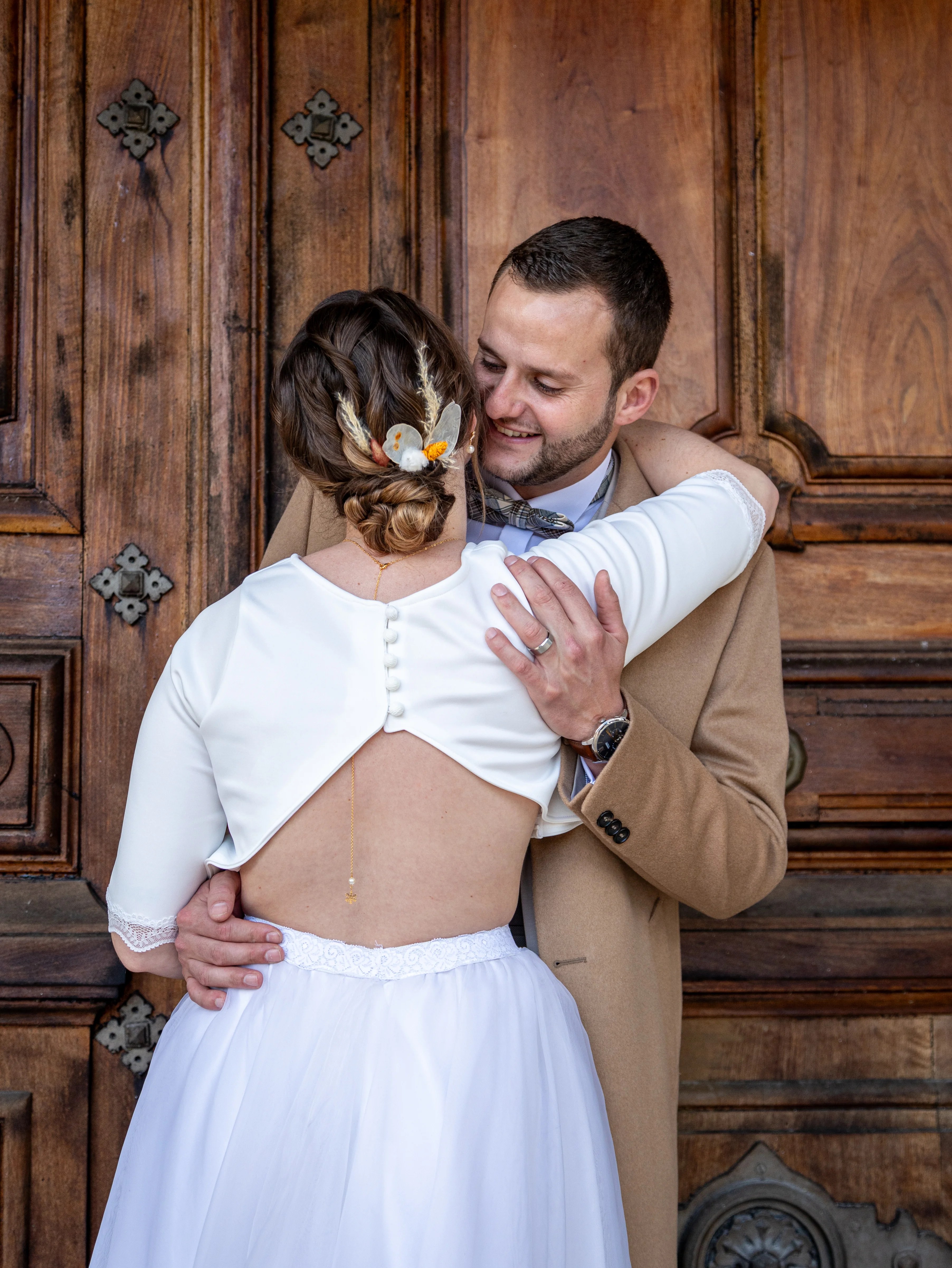 Mariés qui s'enlaçent devant une porte en bois au Clos de Florie vers Chambéry photographiés par Marine Bourely Photographe