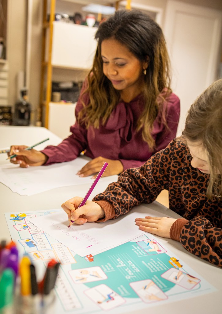 Une femme et une enfant écrivent chacune sur une feuille sur le même bureau photographiée par Marine Bourely Photographe
