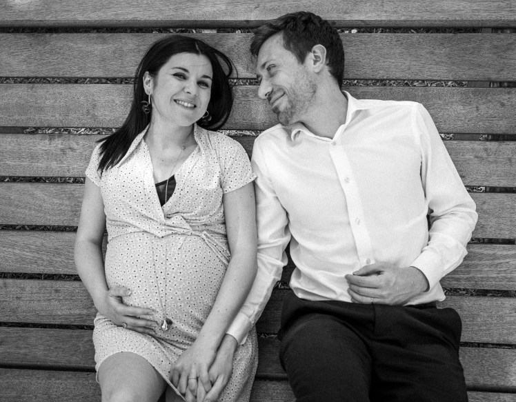 Femme enceinte tient la main de son conjoint amoureux sur un banc à Annecy photographiés par Marine Bourely photographe