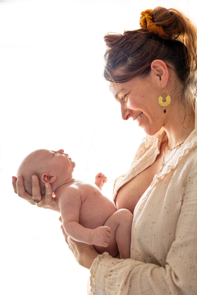 Mère tenant son nouveau-né nu dans ses bras en le regardant avec amour photographiés par Marine Bourely Photographe
