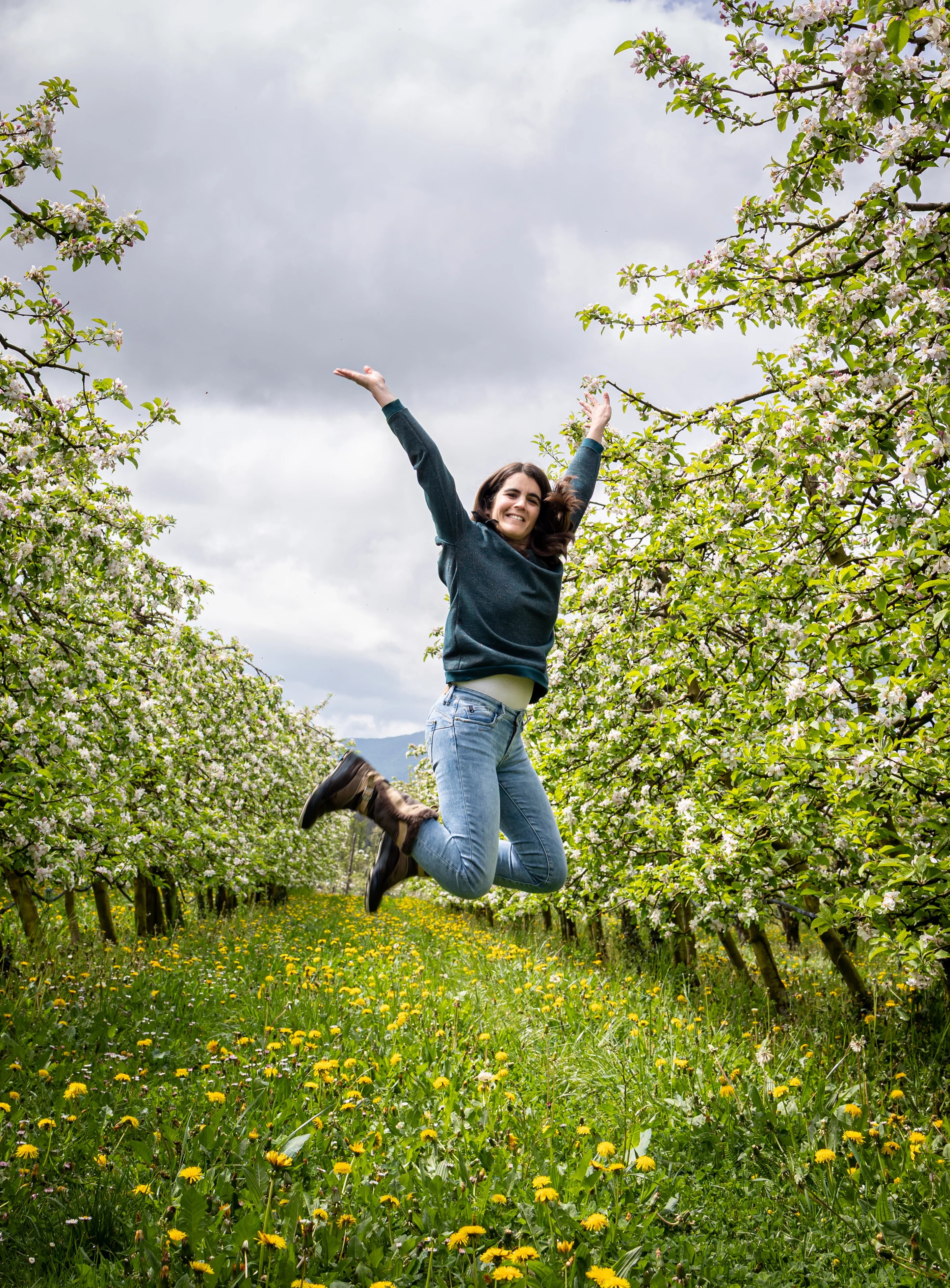 Femme sautant de joie dans un champ d'arbres fruitiers proche d'Annecy photographiée par Marine Bourely Photographe